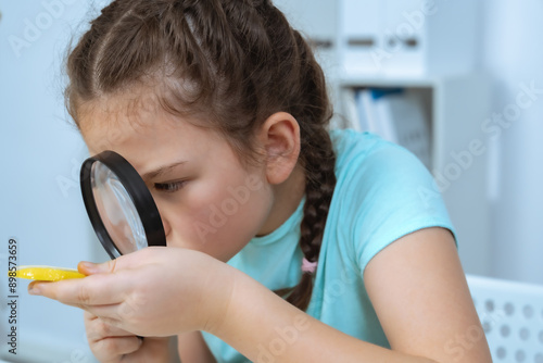 Fotografi A young girl intensely examines a specimen using a magnifying glass, demonstrating her curiosity and interest in scientific exploration