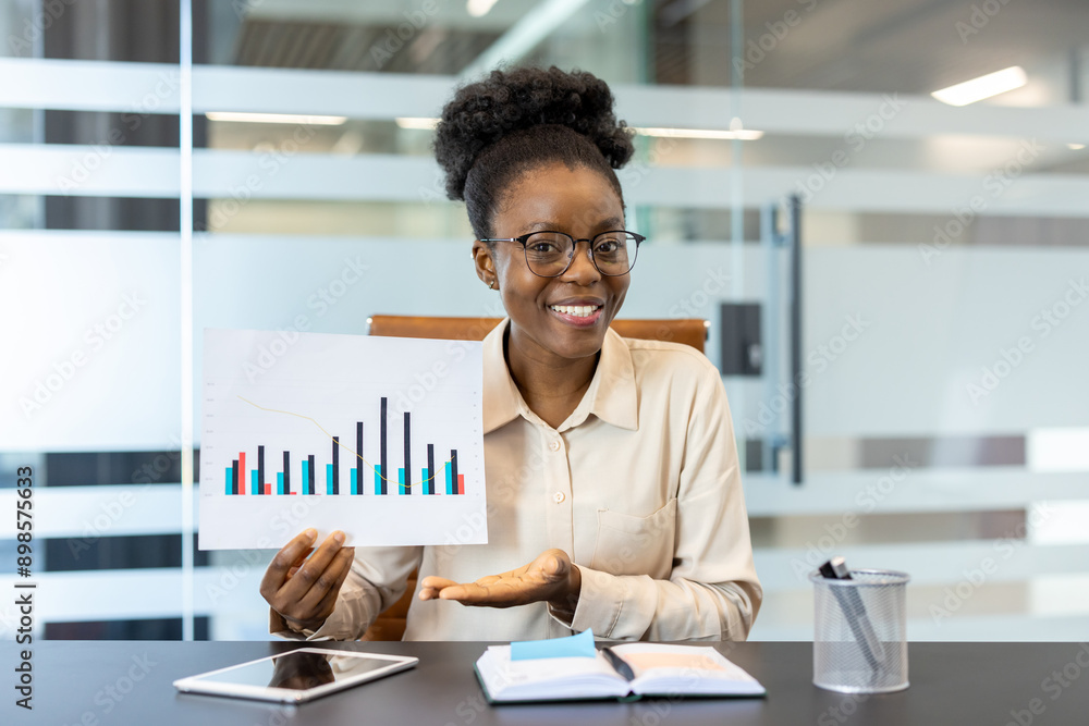 Smiling businesswoman showing financial chart during office meeting. Confident professional explaining business performance with graph. Modern office environment with tablet and documents on desk. Smiling businesswoman showing financial chart during office meeting. Confident professional explaining business performance with graph. Modern office environment with tablet and documents on desk.