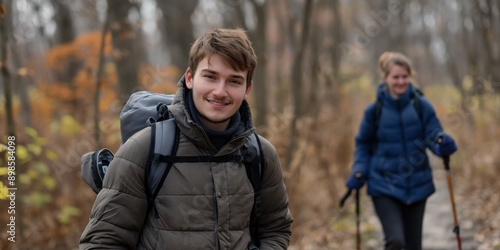 Photo of a young couple hiking on a nature trail, smiling and holding walking poles. Hiking and outdoor adventure concept. 