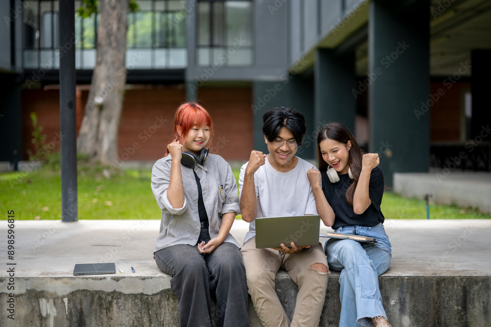 Obraz premium Three young people are sitting on a cement ledge, one of them holding a laptop
