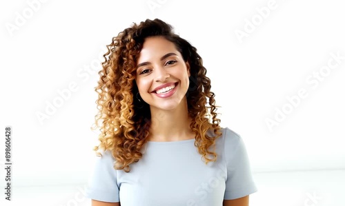 Cheerful young adult woman with curly hair and smiling face standing in studio against white background