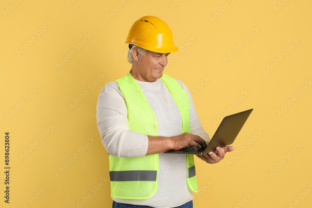 Engineer in hard hat with laptop on yellow background Engineer in hard hat with laptop on yellow background
