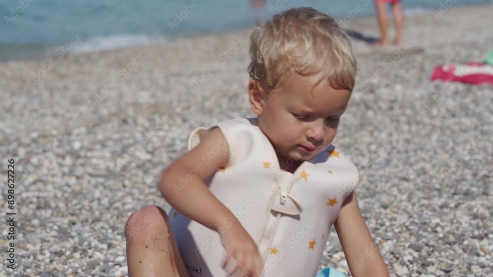 Happy little boy in swim vest life jacket playing on summer beach swimming in sea. Cute child in float lifejacket learning to swim in water. Yevpatoriya, Crimea, Russia 2024 Happy little boy in swim vest life jacket playing on summer beach swimming in sea. Cute child in float lifejacket learning to swim in water. Yevpatoriya, Crimea, Russia 2024