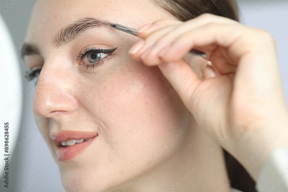 Young woman plucking eyebrow with tweezers on light background, closeup Young woman plucking eyebrow with tweezers on light background, closeup