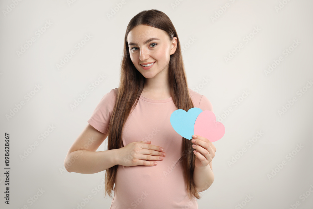 Expecting twins. Pregnant woman holding two paper cutouts of hearts on light grey background Expecting twins. Pregnant woman holding two paper cutouts of hearts on light grey background