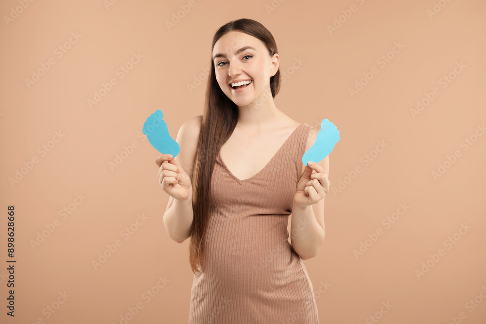 Expecting twins. Pregnant woman holding two paper cutouts of feet on light brown background Expecting twins. Pregnant woman holding two paper cutouts of feet on light brown background
