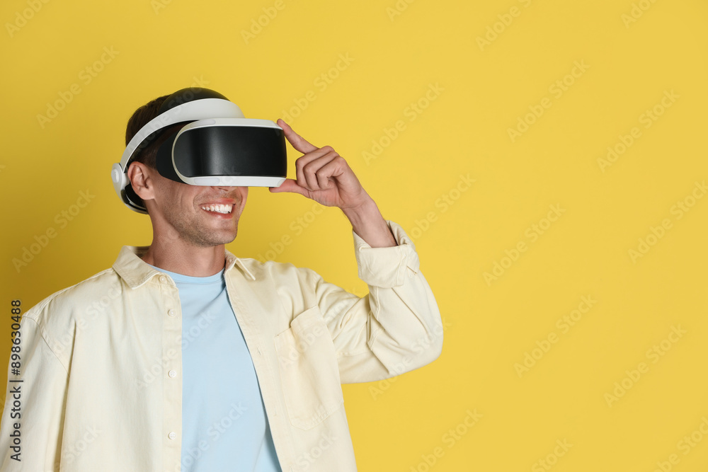 Smiling man using virtual reality headset on yellow background, space for text Smiling man using virtual reality headset on yellow background, space for text