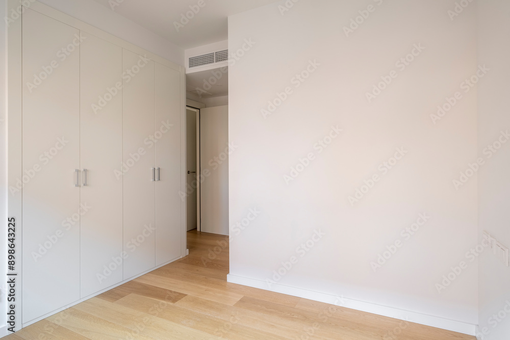 A minimalist bedroom featuring a built-in wardrobe with white doors, natural wood floor, and a wall ventilation system creating a modern and clean look. A minimalist bedroom featuring a built-in wardrobe with white doors, natural wood floor, and a wall ventilation system creating a modern and clean look.