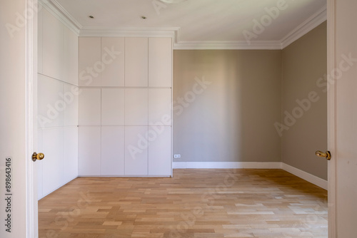 An empty room featuring light wooden flooring, white built-in storage cabinets, and softly colored walls, offering a blank canvas for interior design and decoration.