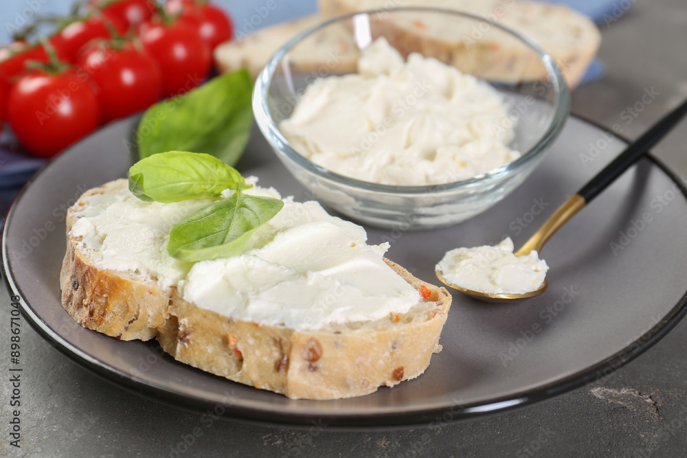 Piece of bread with cream cheese and basil leaves on gray table, closeup Piece of bread with cream cheese and basil leaves on gray table, closeup
