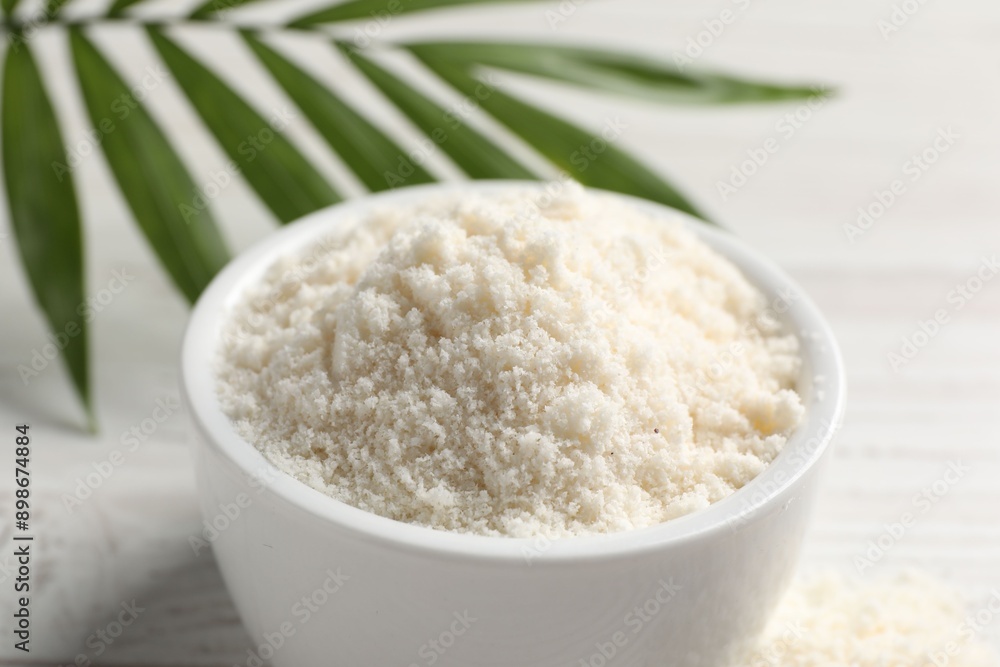 Fresh coconut flour in bowl and palm leaf on white table, closeup Fresh coconut flour in bowl and palm leaf on white table, closeup