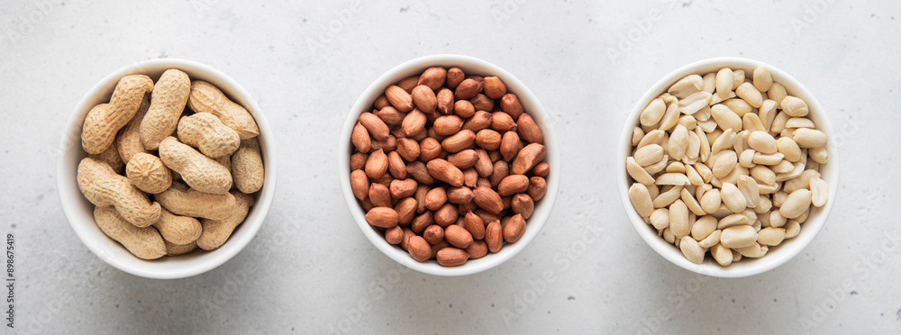 Whole and peeled with blanched and salted peanut nuts in bowls on light background.Top view. Whole and peeled with blanched and salted peanut nuts in bowls on light background.Top view.