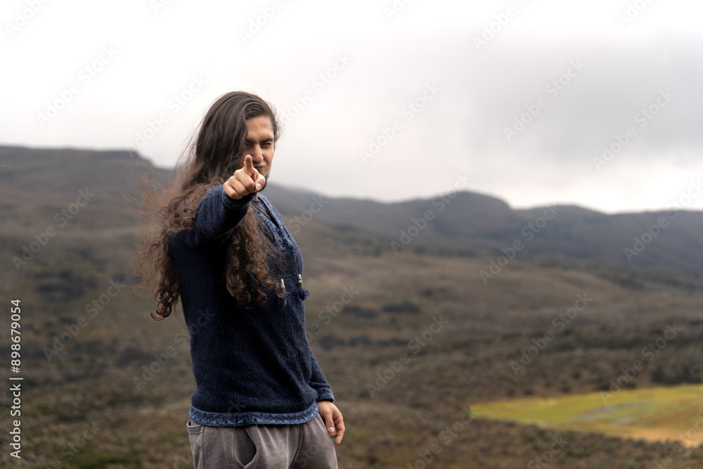 latin male traveler with long hair and beard pointing to the viewer wearing clothes that have indian patterns latin male traveler with long hair and beard pointing to the viewer wearing clothes that have indian patterns