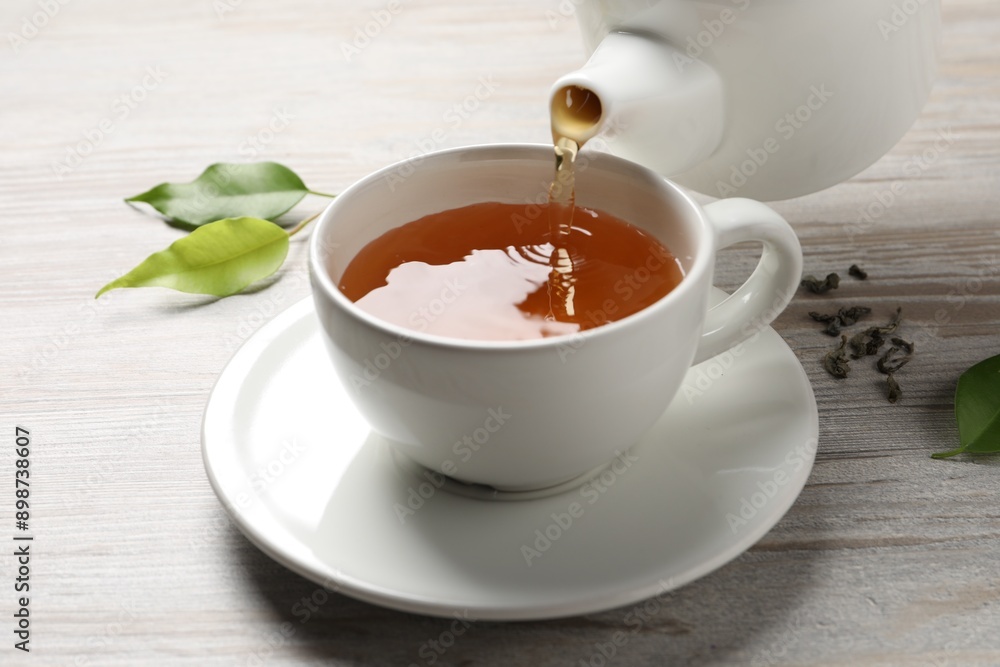 Pouring refreshing green tea into cup at grey wooden table, closeup Pouring refreshing green tea into cup at grey wooden table, closeup