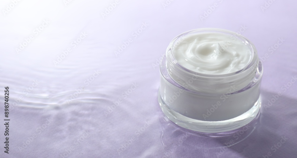 Jar with face cream in water on light violet background, space for text Jar with face cream in water on light violet background, space for text