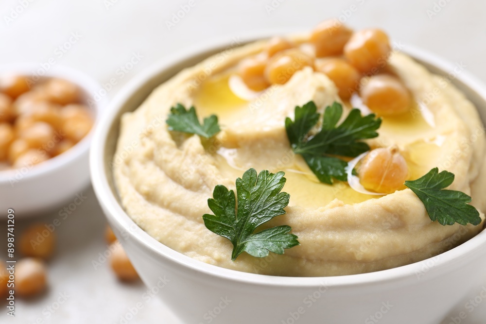 Delicious hummus with olive oil, chickpeas and parsley in bowl on table, closeup Delicious hummus with olive oil, chickpeas and parsley in bowl on table, closeup