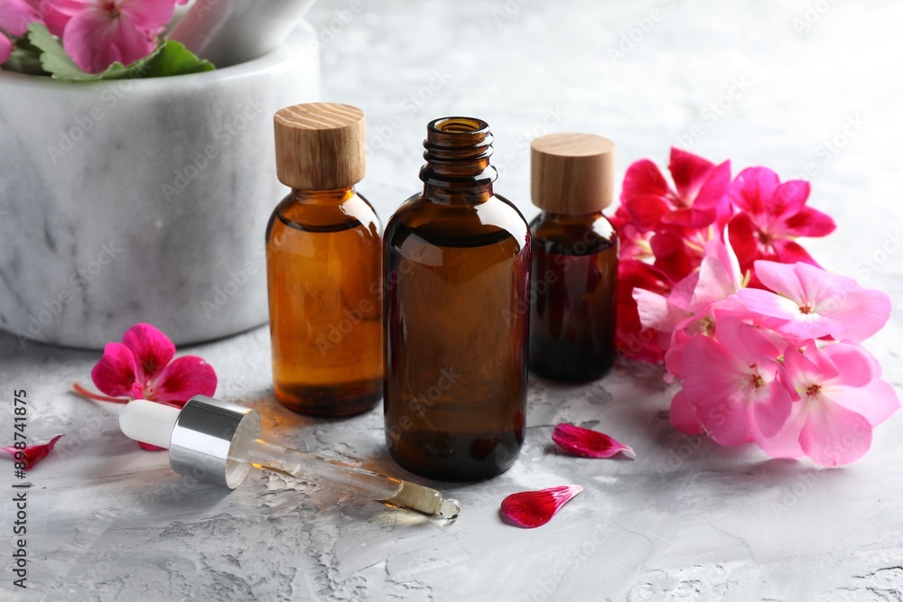 Geranium essential oil in bottles, pipette and beautiful flowers on light grey textured table Geranium essential oil in bottles, pipette and beautiful flowers on light grey textured table