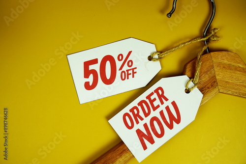 Order Now and Sale 50% on price tag with wooden clothes hanger top view on yellow background photo