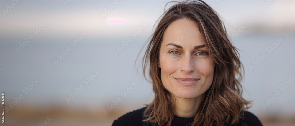 A tight shot of an individual with lengthy locks wearing a black top, framed against a backdrop of still water A tight shot of an individual with lengthy locks wearing a black top, framed against a backdrop of still water