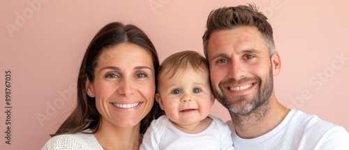  A man, a woman, and a smiling baby stand before a pink wall for a photo