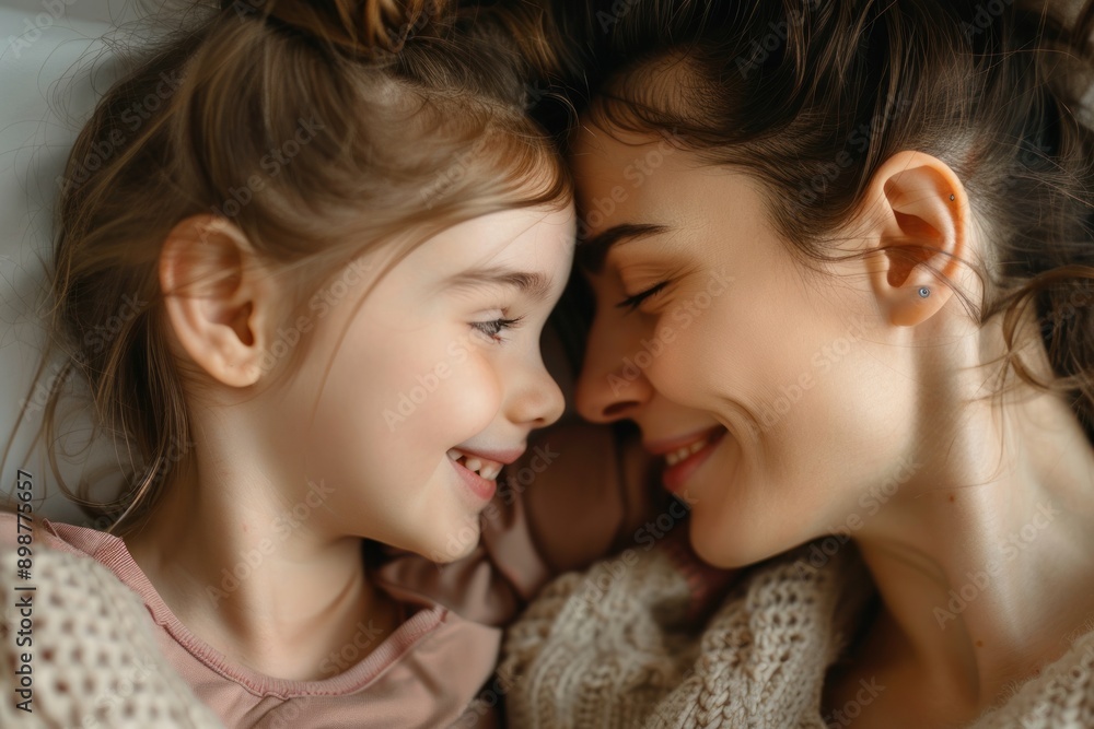 Close up joyful little daughter touch her loving mother face, lying together on bed, looking at each other Close up joyful little daughter touch her loving mother face, lying together on bed, looking at each other
