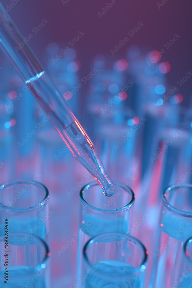 Dripping liquid from pipette into test tube on color background, closeup Dripping liquid from pipette into test tube on color background, closeup