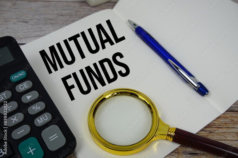 Mutual funds text message written on note page with calculator and magnifying glass top view on wooden background Mutual funds text message written on note page with calculator and magnifying glass top view on wooden background