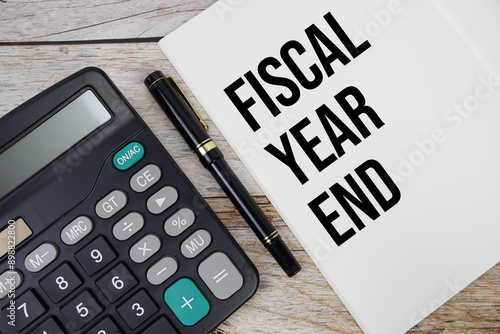 Fiscal Year End text message written on note page with calculator top view on wooden background