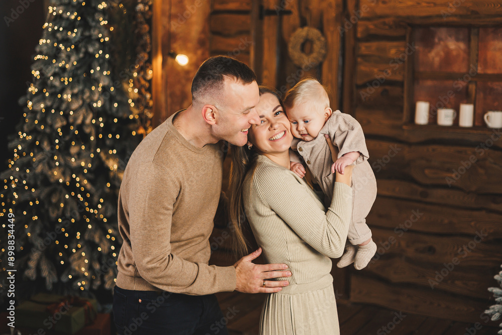 A happy family couple with a child in their arms on the background of a Christmas tree. New Year with a baby. Family New Year's atmosphere. A happy family couple with a child in their arms on the background of a Christmas tree. New Year with a baby. Family New Year's atmosphere.