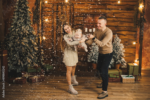 A young mother and father are standing with a small child near a Christmas tree. New Year's family holiday. © Дмитрий Ткачук