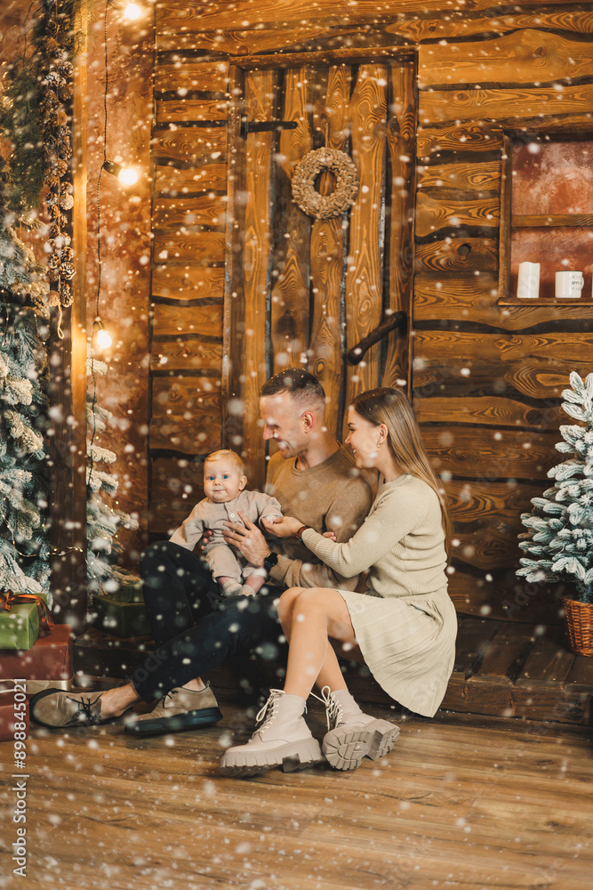 Obraz premium A family with a child on the background of a Christmas tree. A young man and a woman with a child in their hands in a New Year's house. Celebrating the new year in a family circle.