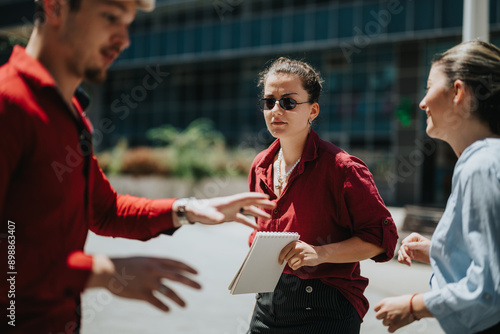 Young business professionals having an outdoor meeting and discussing strategies. A woman is holding a notebook and wearing sunglasses.