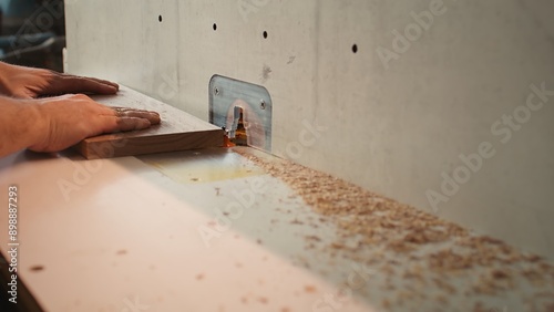 Carpenter in studio puts wood block through spindle moulder, creating smooth edges on wooden pieces. Cabinetmaker in joinery using heavy machinery to craft joints for furniture, camera B close up