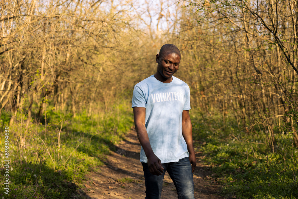 African american climate change volunteer leaving the clean forest area, feeling satisfied with his group work and perseverance. Happy smiling activist finishing litter cleanup. African american climate change volunteer leaving the clean forest area, feeling satisfied with his group work and perseverance. Happy smiling activist finishing litter cleanup.
