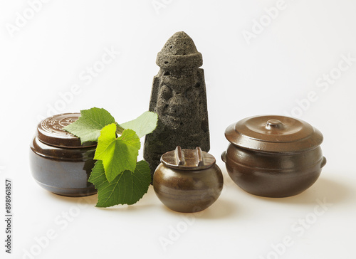 Close-up of three type earthen jars and lid with grape leaf and miniature of Dolhareubang(stone grandfather) on white floor, South Korea
 photo