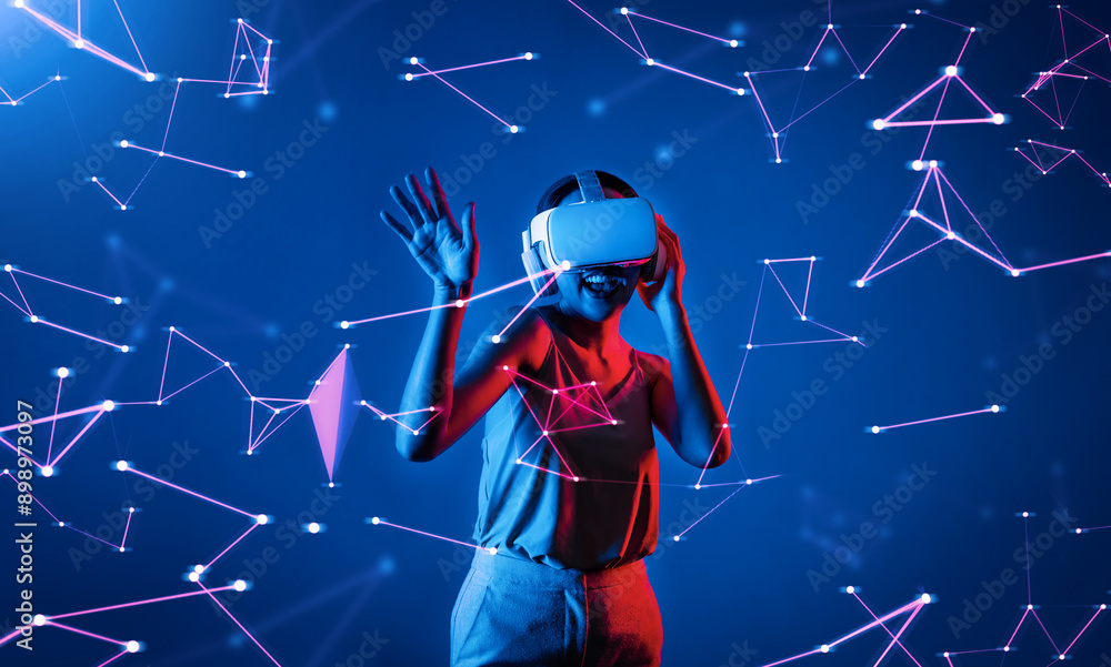 Fototapeta premium Female standing wearing white VR headset and tank top connecting metaverse, future cyberspace community technology, enjoy dancing in cyberpunk neon light gesticulate hand and body. Hallucination.