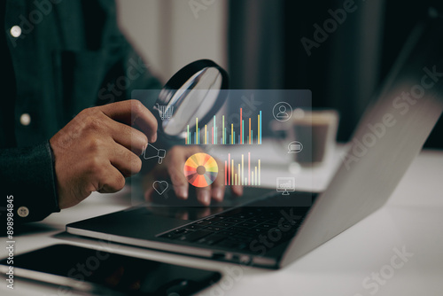 Fotografie Person using a magnifying glass to examine data visualizations on a laptop