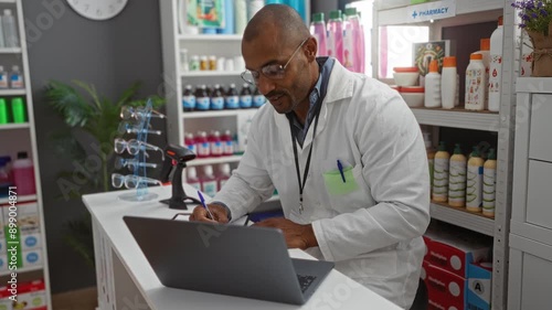 Wallpaper Mural Pharmacist working on laptop and writing notes in a well-stocked pharmacy with shelves of products and glasses display Torontodigital.ca