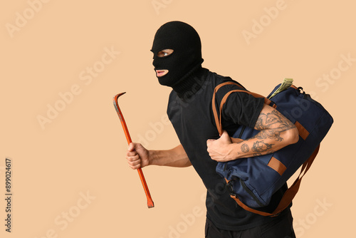 Male thief with crowbar and bag of money on beige background photo