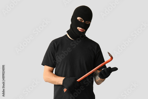 Male thief with crowbar on grey background