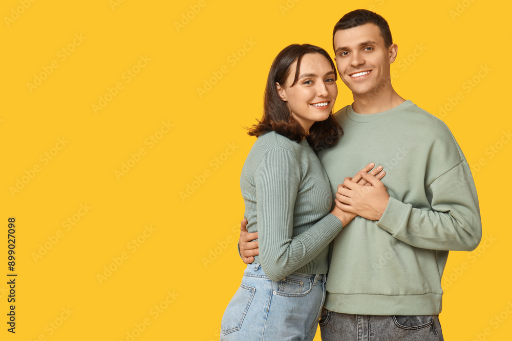 Fototapeta premium Cheerful young couple hugging on yellow background