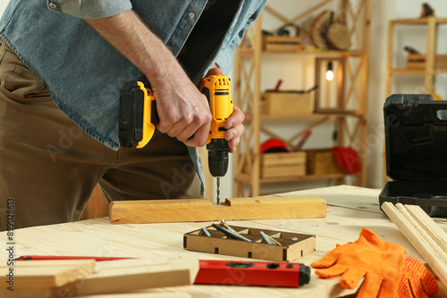 Craftsman working with drill at wooden table in workshop, closeup