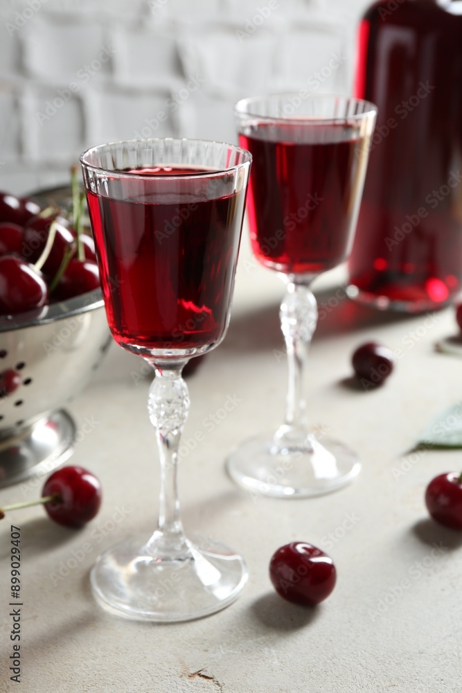Delicious cherry liqueur in glasses and fresh berries on light grey table Delicious cherry liqueur in glasses and fresh berries on light grey table