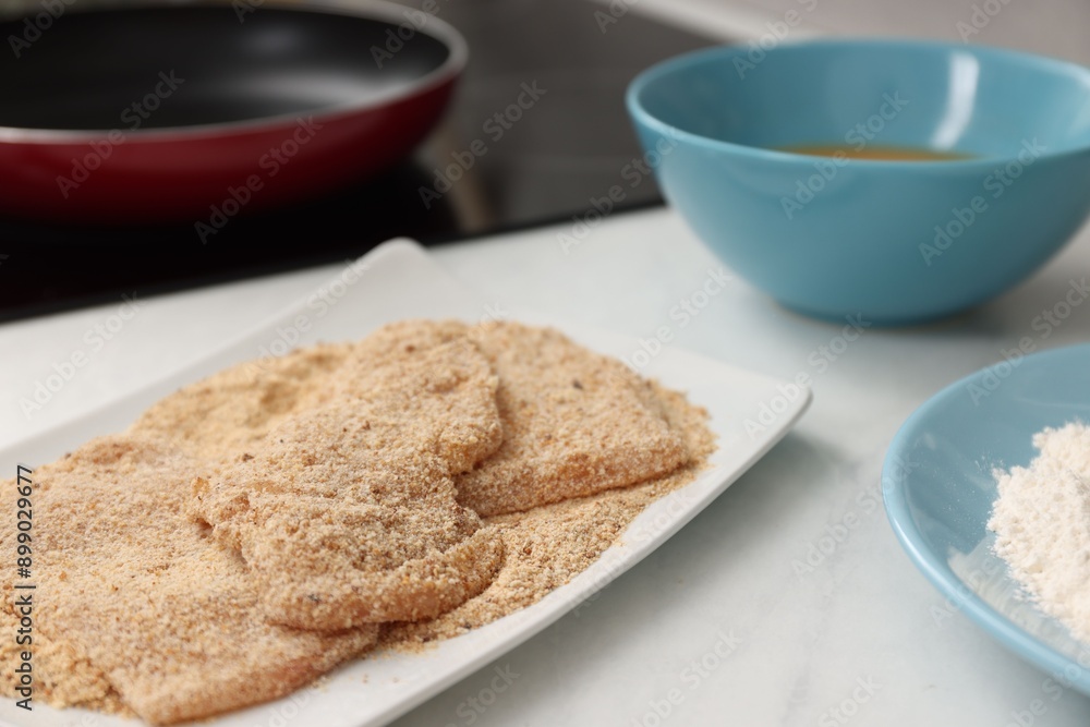 Making schnitzels. Raw meat with bread crumbs on white table, closeup Making schnitzels. Raw meat with bread crumbs on white table, closeup