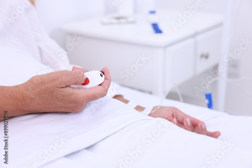 Senior woman pressing emergency call button on bed in hospital, closeup