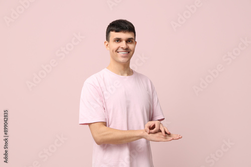 Young deaf mute man using sign language on pink background