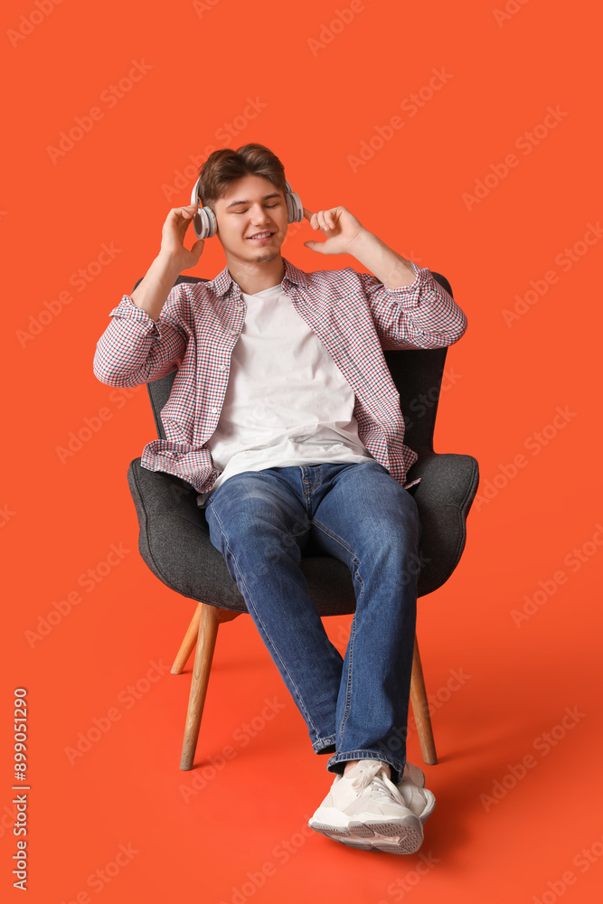 Handsome young man in headphones sitting in armchair on orange background Handsome young man in headphones sitting in armchair on orange background