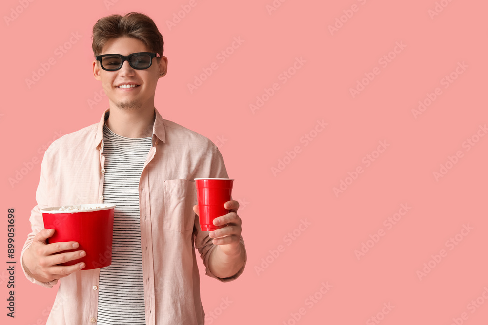 Handsome young man in 3D glasses holding bucket with popcorn and plastic cup of cola on pink background Handsome young man in 3D glasses holding bucket with popcorn and plastic cup of cola on pink background