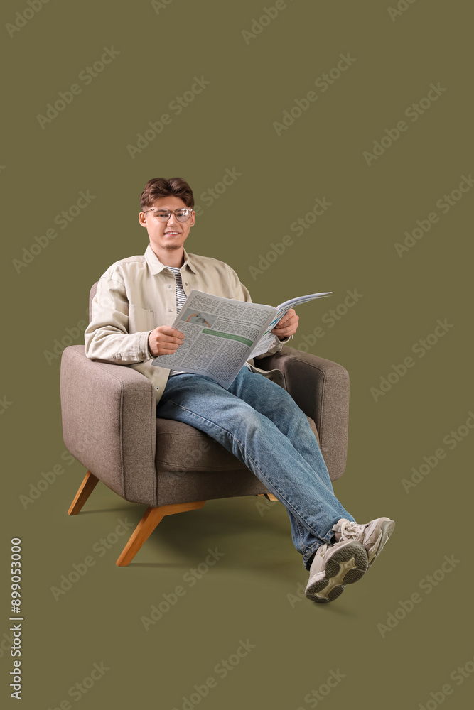 Handsome young man reading newspaper and sitting in armchair on green background Handsome young man reading newspaper and sitting in armchair on green background