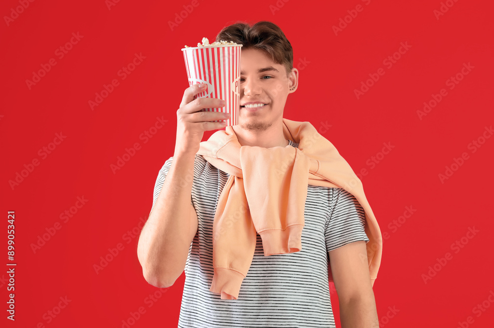 Handsome young man holding bucket with popcorn on red background Handsome young man holding bucket with popcorn on red background